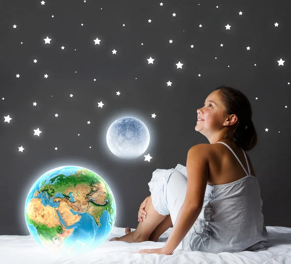 女孩坐在床上，看着地球的行星 — 图库照片