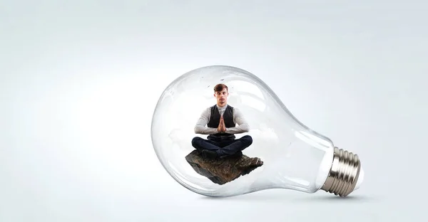 Бізнесмен робить йогу в лотосі позують всередині лампочки. Змішані носії — стокове фото