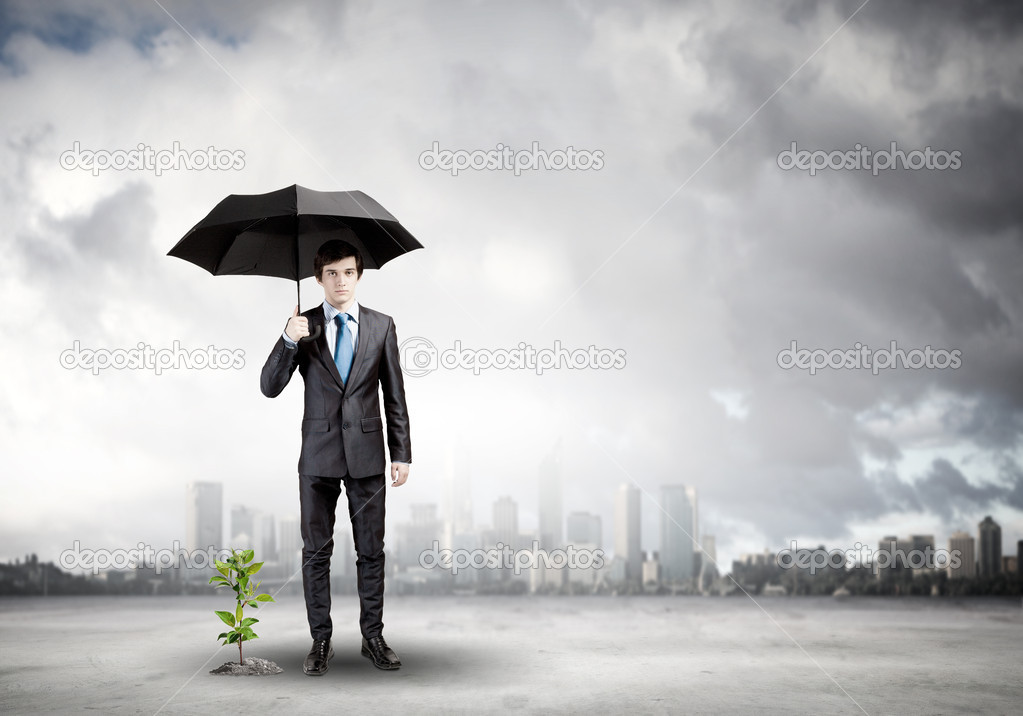 Businessman protecting sprout with umbrella