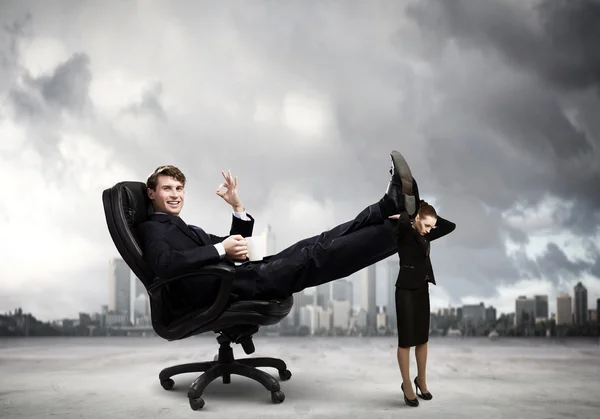 Businessman sitting in chair with legs on colleague — Stock Photo, Image