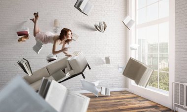 Genç bir kadın kitap okurken havada duruyor.