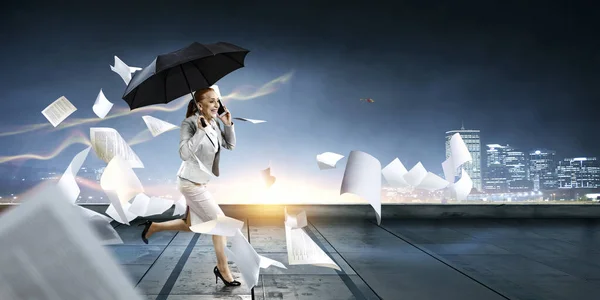 Businesswoman running with umbrella . Mixed media — Stock Photo, Image