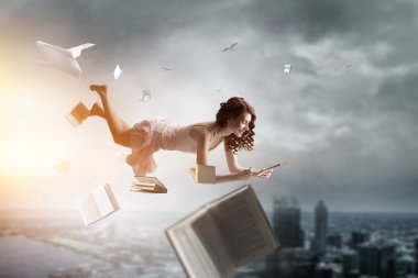 Genç bir kadın kitap okurken havada duruyor.
