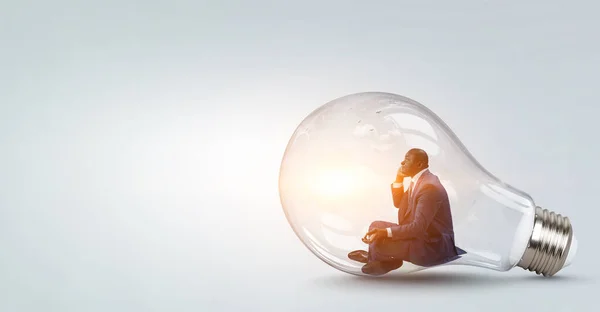 Jovem negro sentado e meditando dentro da lâmpada — Fotografia de Stock