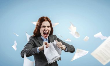 Genç, stresli bir kadın işe kızgın, yüz ifadesiyle belgeleri yırtıyor. Karışık ortam