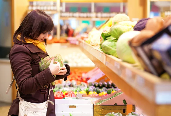 Vackra flickan välja kronärtskockor på marknaden — Stockfoto