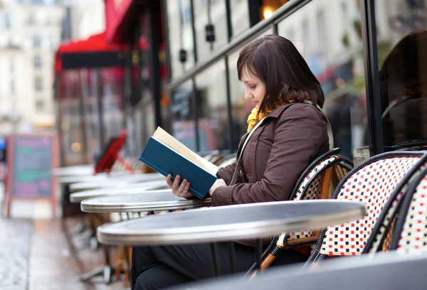 Hermosa joven leyendo un libro en la cafetería de la calle parisina — Foto de Stock