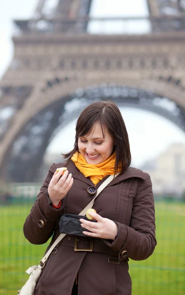 Szczęśliwa młoda kobieta jedzenie makaroniki w pobliżu Wieży Eiffla — Zdjęcie stockowe
