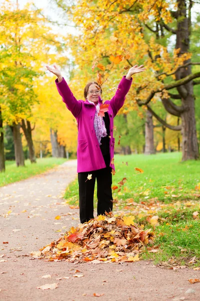 Alegre mujer de mediana edad jugando con hojas de otoño por el otoño —  Fotos de Stock