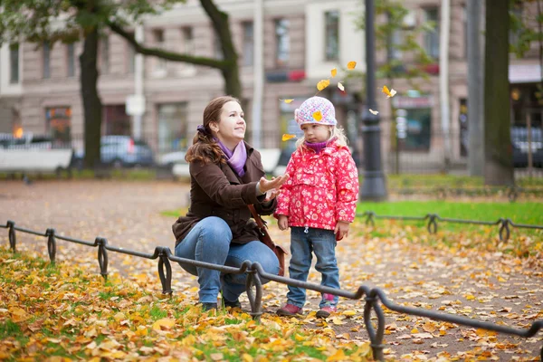 Moeder en haar dochtertje spelen met gele bladeren — Stockfoto