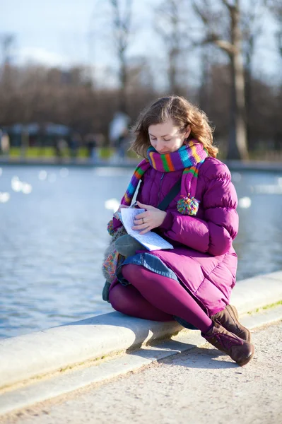 Досить молода дівчина щось пише в записнику на відкритому повітрі — стокове фото