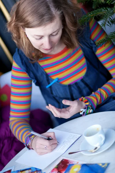 Kafede kartpostal yazma parlak giysiler içinde güzel bir kız — Stok fotoğraf