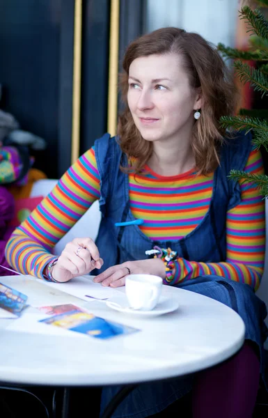 Belle fille en vêtements lumineux écrivant des cartes postales dans un café — Photo