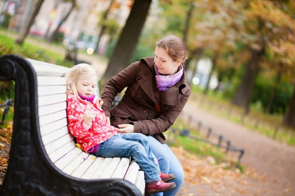 Beautiful mother and daughter sitting on a bench by fall — Stock Photo, Image