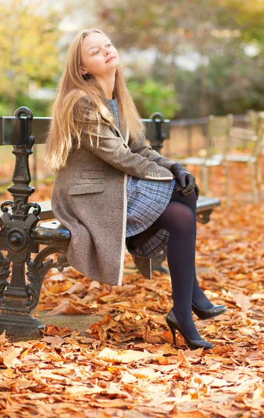 Pretty young lady sitting on the bench and enjoying autumn day — Stock Photo, Image
