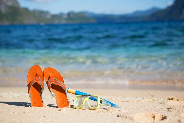 Tofflor, mask och snorkel på sandstrand nära vattnet — Stockfoto