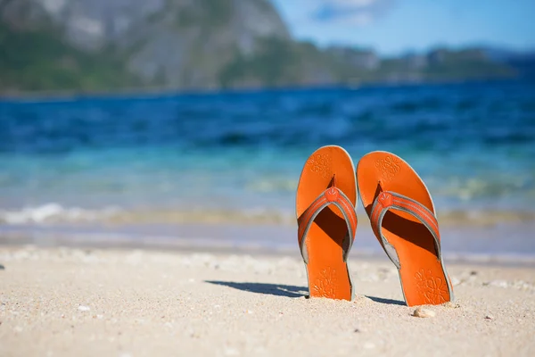 Slippers op zand strand in de buurt van het water — Stockfoto