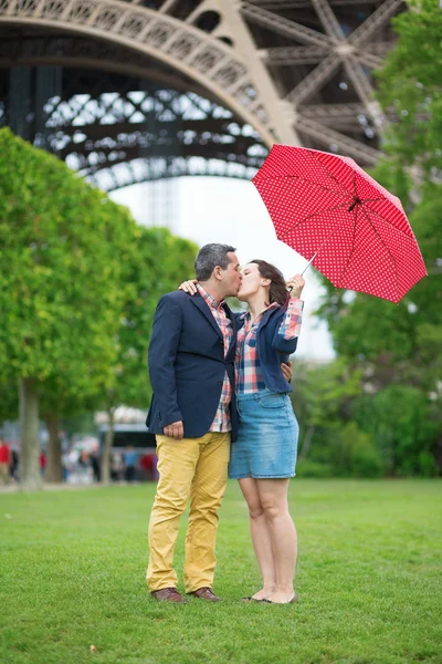 Casal com guarda-chuva vermelho sob a torre Eiffel — Fotografia de Stock