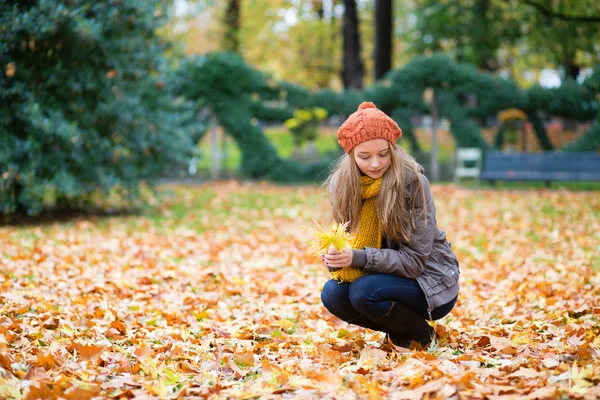 Chica recogiendo hojas de otoño en un parque — Foto de Stock