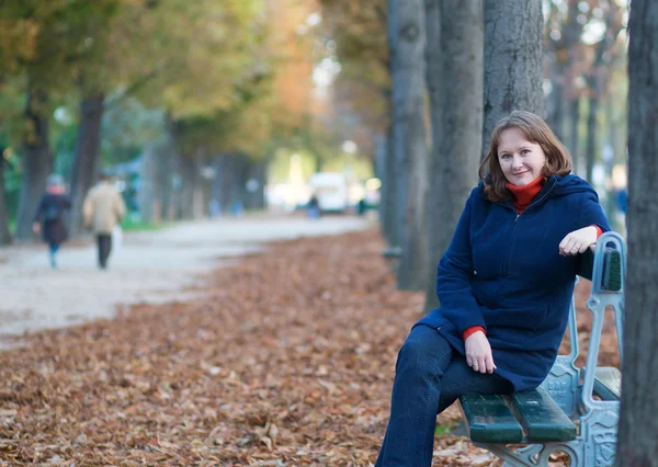 Mädchen sitzt an einem Herbsttag auf der Bank im Park — Stockfoto