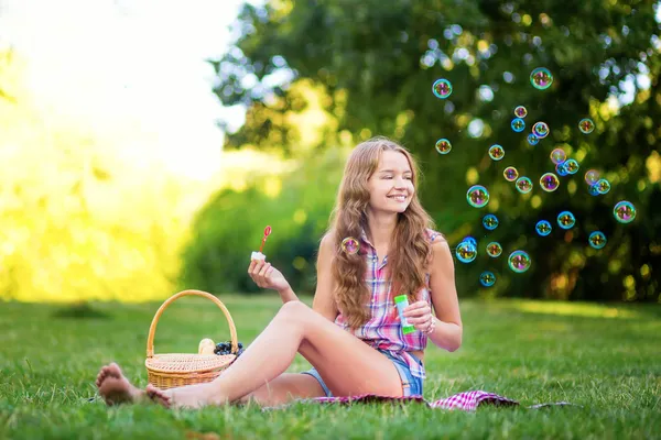 Chica joven sentada en la hierba soplando burbujas —  Fotos de Stock