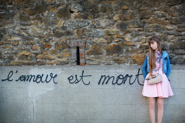 Sad girl near the wall with words "Love is dead" — Stock Photo, Image