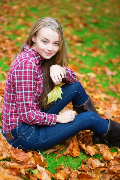 Dívka sedící na zemi v pádu park — Stock fotografie