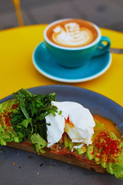 Mavi fincanda süt çizilmiş taze beyaz kahve ve sarı masada avokado ve yumurtalı Benedict.