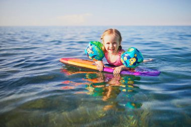Fransa 'da Akdeniz' de su kanatlarıyla yüzen mutlu küçük kız. Neşeli çocuk denizde tatilin tadını çıkarıyor. Çocuklar için açık hava yaz etkinlikleri
