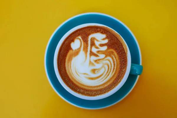 Чашка Свежего Белого Кофе Молоком Рисунок Синей Чашке Желтый Стол — стоковое фото