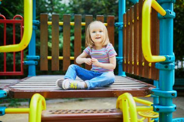 Güneşli bir günde oyun bahçesinde sevimli küçük bir kız. Anaokulu çocuğu kaydırağın üstünde oynuyor. Çocuklar için açık hava aktiviteleri