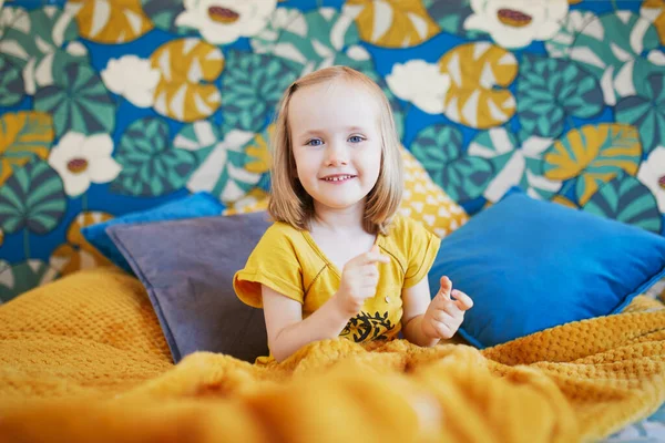 Güzel dekore edilmiş yatak odasında, yatakta oturan sevimli, oynak küçük kız.