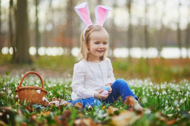 Tavşan kulaklı bir kız Paskalya 'da yumurta avı oynuyor. Bir sürü kartopu çiçeğiyle çimenlerde oturan ve renkli yumurtaları sepette toplayan bir çocuk. Paskalyayı dışarıda kutlayan küçük çocuk.