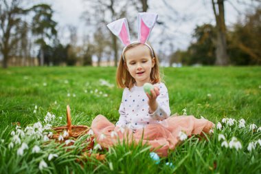 Tavşan kulaklı bir kız Paskalya 'da yumurta avı oynuyor. Anaokulu öğrencisi çimenlerde oturmuş, elinde bir sürü kartopu çiçeğiyle çikolatalı tavşancık yiyor. Paskalyayı parkta ya da ormanda kutlayan küçük bir çocuk.
