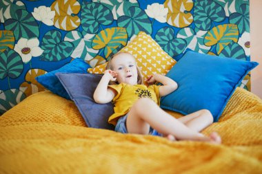 Güzel dekore edilmiş yatak odasında, yatakta oturan sevimli, oynak küçük kız.