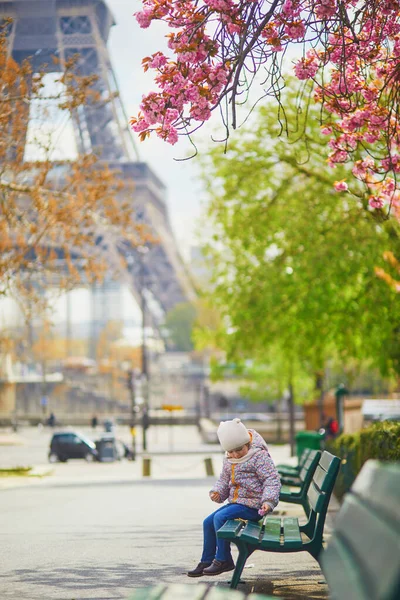 可爱的三岁小女孩坐在法国巴黎埃菲尔铁塔附近的长椅上 在春天的一天 樱桃树在巴黎盛开 — 图库照片