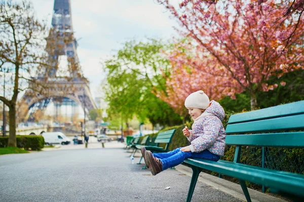 パリのエッフェル塔の近くのベンチに座っている愛らしい3歳の少女 春の日にパリで満開の桜 — ストック写真