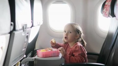 Uçakla seyahat ederken yemek kutusundan abur cubur yiyen 4 yaşında bir kız. Uçuş sırasında çocuklar için sağlıklı yiyecekler.