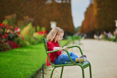 Paris 'te, Tuileries bahçesinde yeşil sandalyede oturan sevimli anaokulu kızı, sonbahar günü. Mutlu çocuk sonbahar gününün tadını çıkarıyor. Fransa 'da sonbahar sezonu. Çocuklar için açık hava sonbahar aktiviteleri
