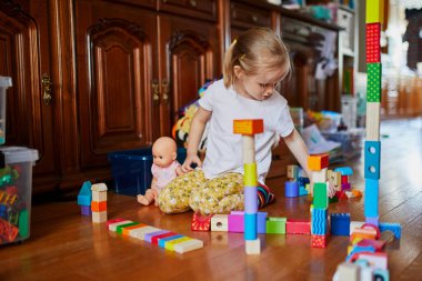 Sevimli prechooler kız yerde oturuyor ve renkli yapı taşlarıyla oynuyor. Çocuklar için ev içi yaratıcı aktiviteler