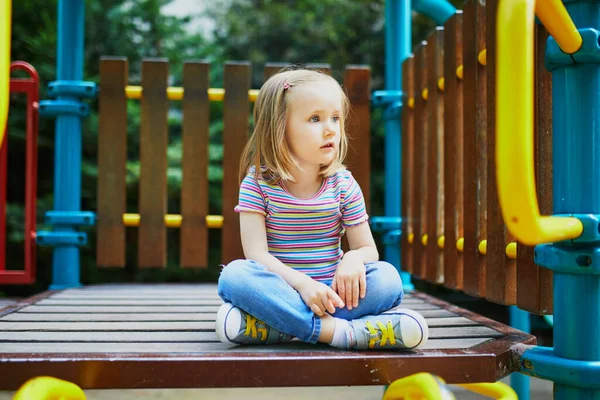 Güneşli bir günde oyun bahçesinde sevimli küçük bir kız. Anaokulu çocuğu kaydırağın üstünde oynuyor. Çocuklar için açık hava aktiviteleri