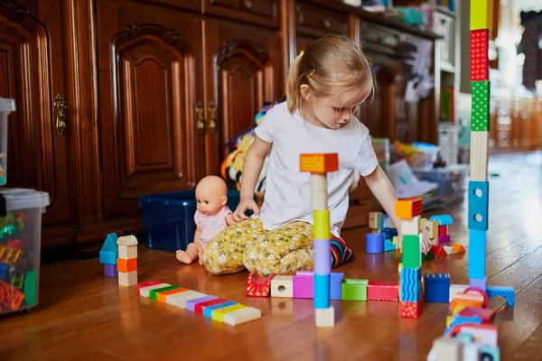 Sevimli prechooler kız yerde oturuyor ve renkli yapı taşlarıyla oynuyor. Çocuklar için ev içi yaratıcı aktiviteler