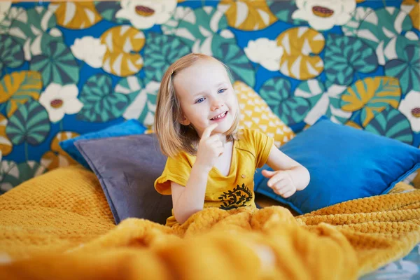 Güzel dekore edilmiş yatak odasında, yatakta oturan sevimli, oynak küçük kız.