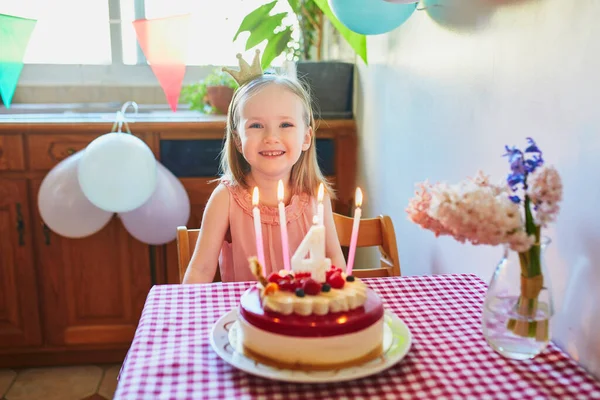 Happy little girl in princess crown celebrating her fourth birthday and making a wish. Little kid with birthday cake and candle