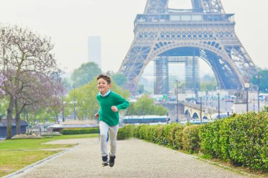 Eyfel kulesinin yakınında koşan bir çocuk. Fransa, Paris 'te eğlenen bir çocuk. Mutlu çocuk dışarıda oynuyor.