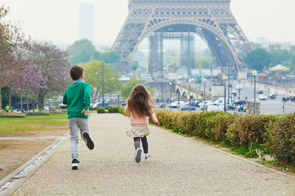 エッフェル塔の近くを走っている男の子と女の子 兄と妹はフランスのパリで楽しんでいます 幸せな兄弟は屋外で遊ぶ — ストック写真
