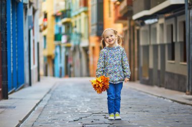 Sevimli anaokulu kızı dışarıda güneşli ve güzel bir sonbahar gününün tadını çıkarıyor. Mutlu çocuk Bermeo, İspanya 'da sonbahar yapraklarını topluyor. Çocuklar için açık hava sonbahar aktiviteleri