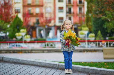 Sevimli anaokulu kızı dışarıda güneşli ve güzel bir sonbahar gününün tadını çıkarıyor. Mutlu çocuk Guernika, İspanya 'da sonbahar yaprakları topluyor. Çocuklar için açık hava sonbahar aktiviteleri