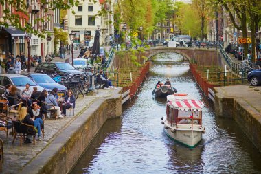 AMSTERDAM, THE NETHERLANDS - MAY 1, 2022: People enjoying nice spring day in Amsterdam with its canals, bridges and boats