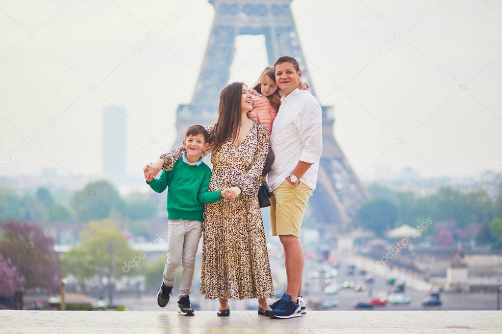 Happy family of four enjoying their trip to Paris, France. Mother, father, son and daughter near the Eiffel tower in Paris. Married couple with kids travelling in France